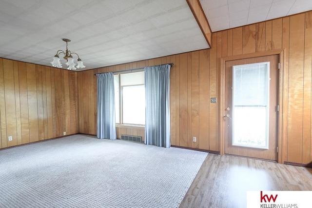 spare room featuring visible vents, wood walls, light wood-style floors, baseboards, and a notable chandelier
