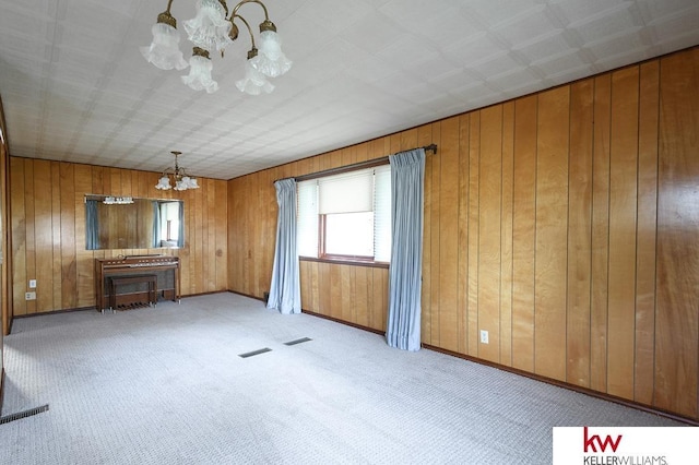unfurnished living room featuring wooden walls, visible vents, a notable chandelier, and carpet