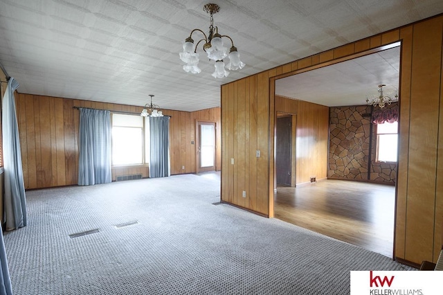 carpeted spare room with wooden walls, a notable chandelier, and visible vents
