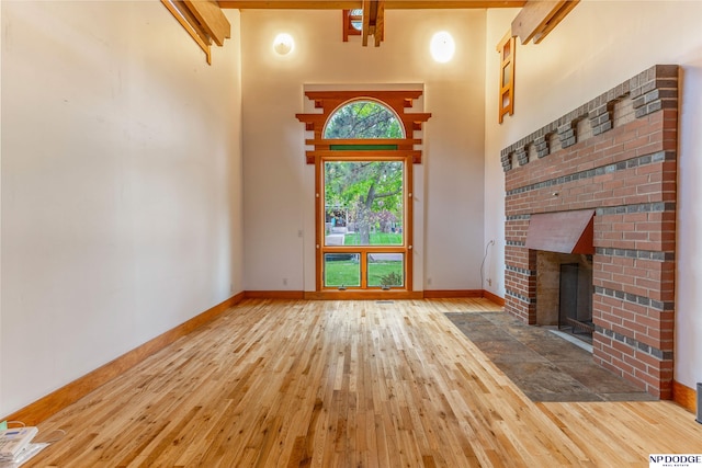 unfurnished living room with baseboards, a high ceiling, a brick fireplace, and hardwood / wood-style floors