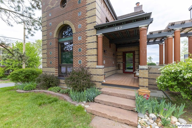 view of exterior entry featuring brick siding, covered porch, and a chimney