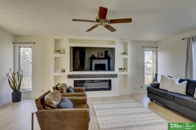 living area featuring built in features, ceiling fan, wood finished floors, and plenty of natural light