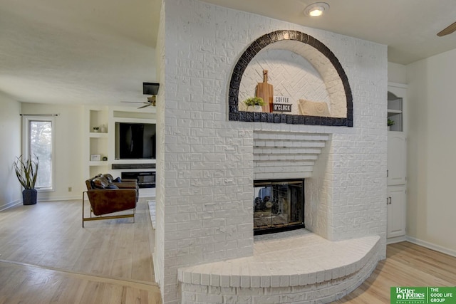 living area featuring a ceiling fan, built in features, a fireplace, and wood finished floors
