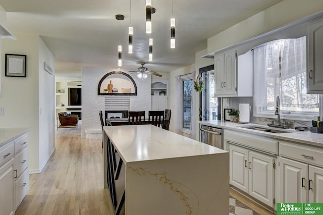 kitchen featuring a sink, a ceiling fan, light wood finished floors, stainless steel dishwasher, and a center island