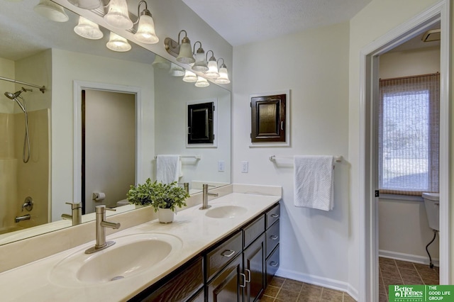 full bathroom with baseboards, double vanity, a sink, and toilet