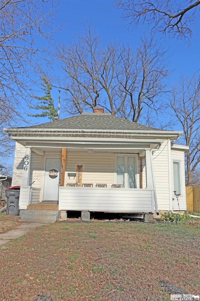 view of front of home featuring covered porch, a front yard, and a chimney