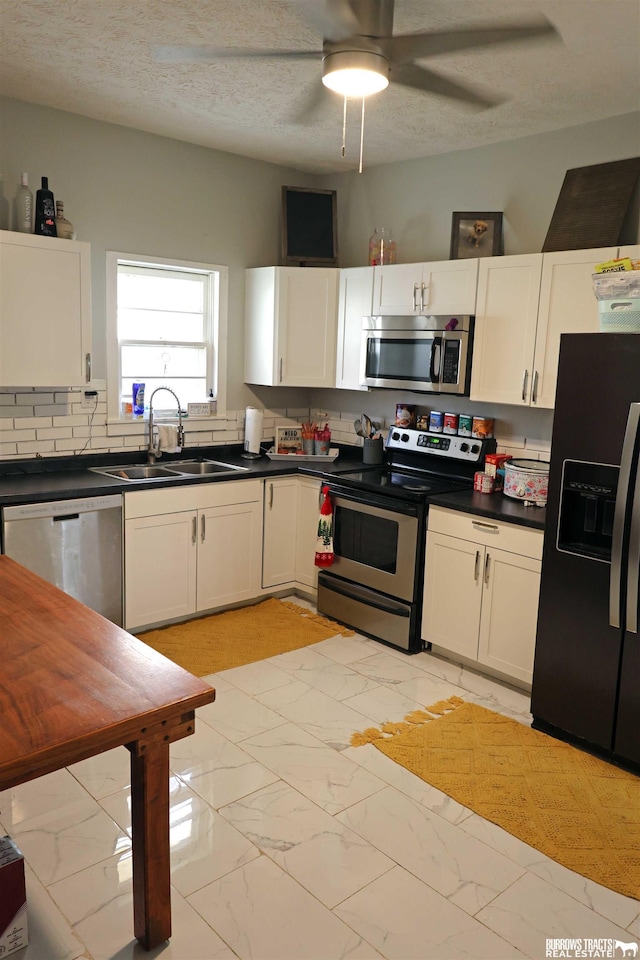 kitchen with white cabinetry, marble finish floor, a sink, dark countertops, and appliances with stainless steel finishes