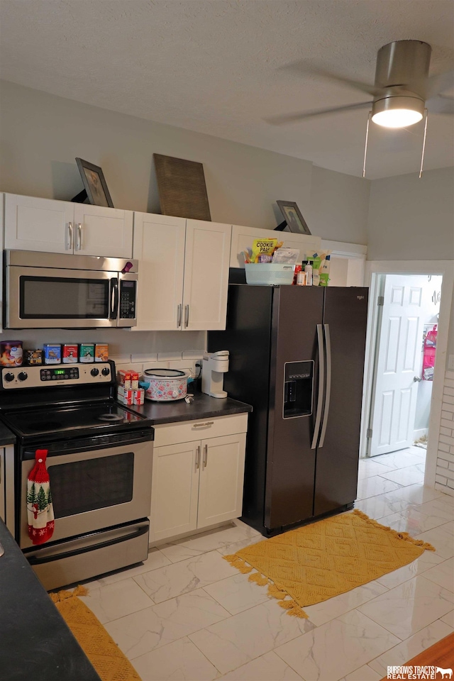 kitchen featuring a ceiling fan, marble finish floor, dark countertops, white cabinets, and appliances with stainless steel finishes
