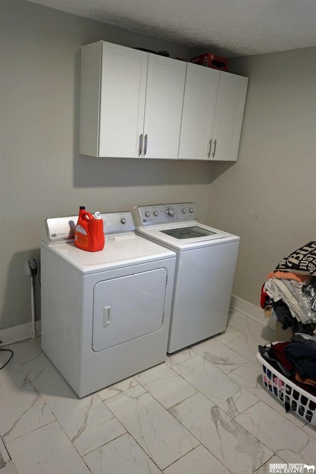 laundry area with baseboards, a textured ceiling, marble finish floor, cabinet space, and washer and dryer