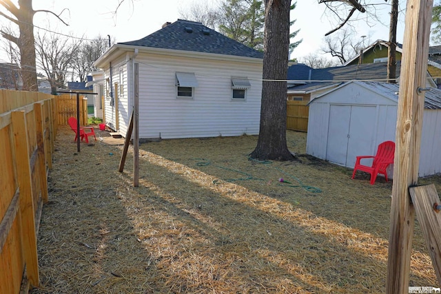 exterior space featuring an outbuilding, a fenced backyard, roof with shingles, and a shed