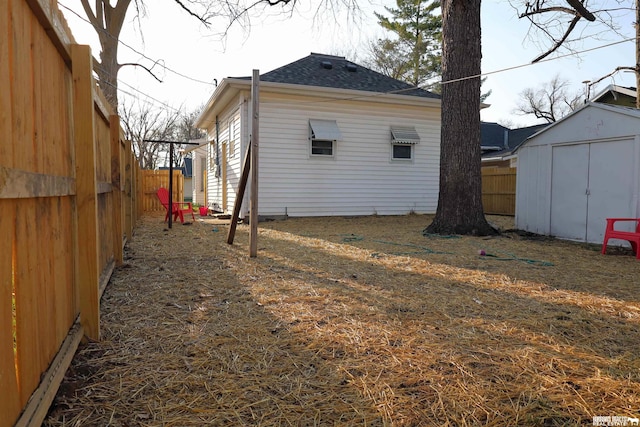view of property exterior featuring an outdoor structure, fence, a storage shed, and roof with shingles