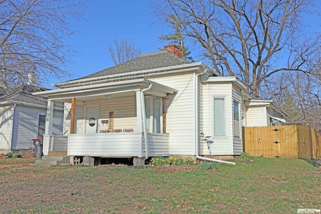 view of front of house featuring covered porch, fence, a front lawn, and a chimney