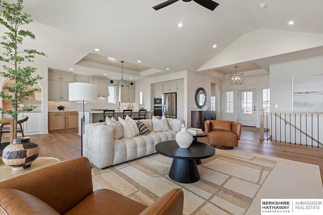 living room featuring recessed lighting, lofted ceiling, ceiling fan with notable chandelier, and light wood-style floors
