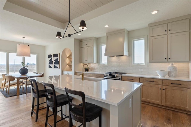 kitchen with a healthy amount of sunlight, stainless steel range with gas stovetop, a sink, light wood-style floors, and custom range hood