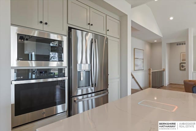 kitchen with light stone countertops, appliances with stainless steel finishes, visible vents, recessed lighting, and vaulted ceiling