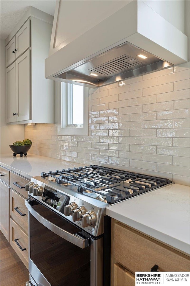 kitchen featuring stainless steel gas range, tasteful backsplash, ventilation hood, and light countertops