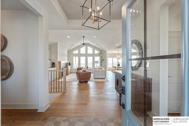 foyer entrance featuring wood-type flooring, baseboards, ceiling fan with notable chandelier, and vaulted ceiling