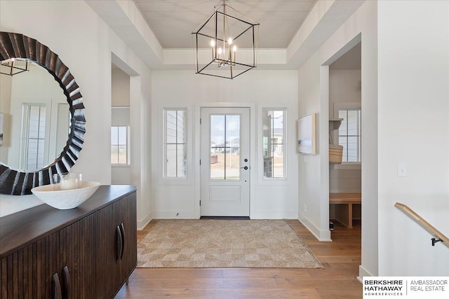entrance foyer featuring baseboards, light wood-type flooring, a raised ceiling, and a chandelier