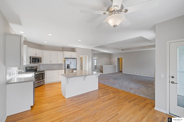 kitchen featuring a sink, a kitchen breakfast bar, appliances with stainless steel finishes, light wood-type flooring, and white cabinets