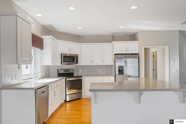 kitchen with a sink, a kitchen bar, appliances with stainless steel finishes, white cabinets, and light wood-style floors