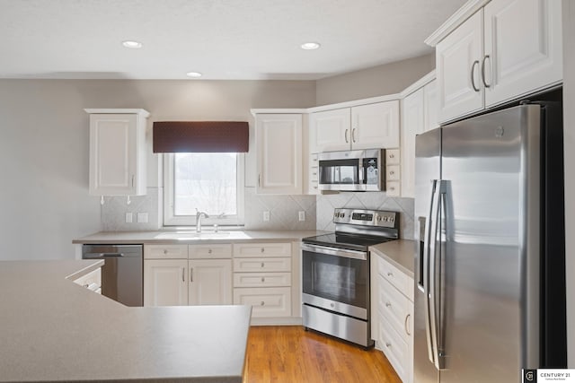 kitchen with white cabinetry, decorative backsplash, a sink, light wood finished floors, and appliances with stainless steel finishes