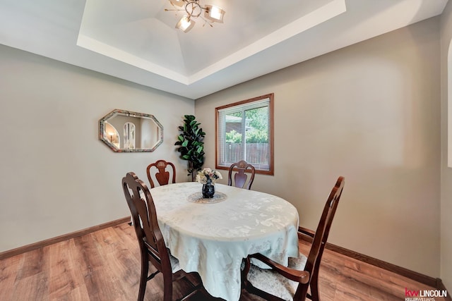 dining area with a tray ceiling, baseboards, and light wood-type flooring