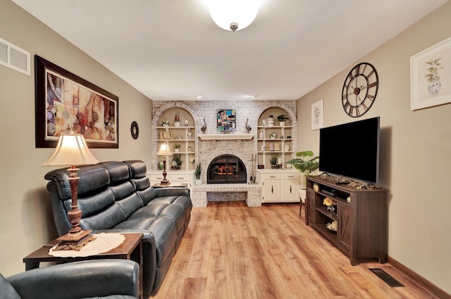 living room featuring light wood-style floors, a fireplace, and built in features