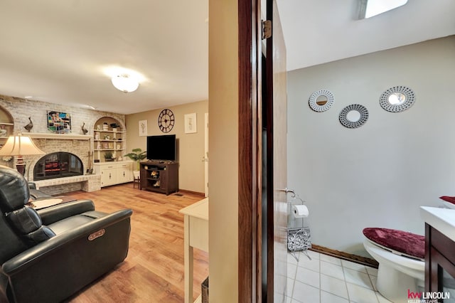 living room featuring a fireplace, built in features, baseboards, and light wood finished floors