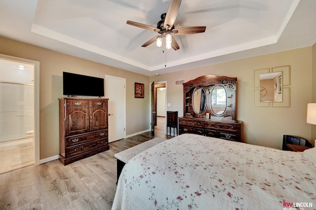 bedroom featuring a tray ceiling, light wood finished floors, baseboards, and ensuite bathroom