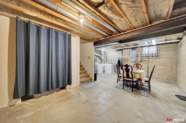 unfinished below grade area with separate washer and dryer, electric panel, stairway, and brick wall