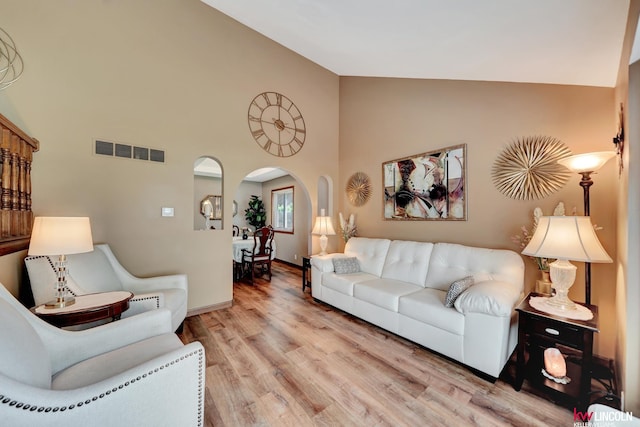 living area with arched walkways, wood finished floors, high vaulted ceiling, and baseboards