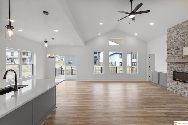 unfurnished living room featuring high vaulted ceiling, a sink, a fireplace, light wood-style flooring, and ceiling fan with notable chandelier