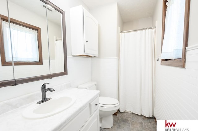 bathroom featuring toilet, stone finish floor, vanity, and a shower with curtain