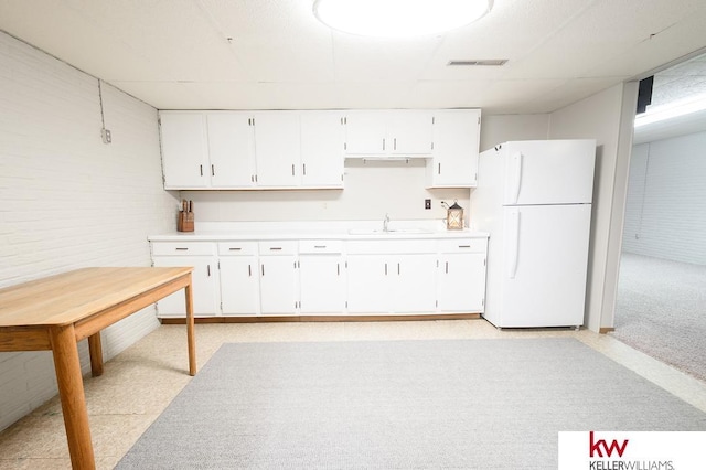 kitchen featuring brick wall, light countertops, freestanding refrigerator, and white cabinetry