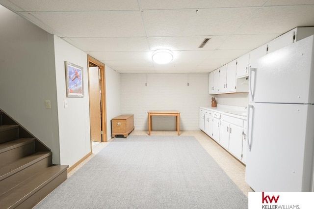 kitchen with light colored carpet, a paneled ceiling, freestanding refrigerator, and white cabinetry