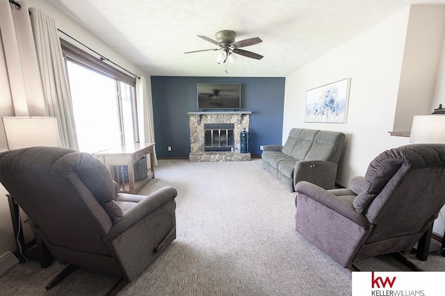 living area with baseboards, carpet, a stone fireplace, and a ceiling fan