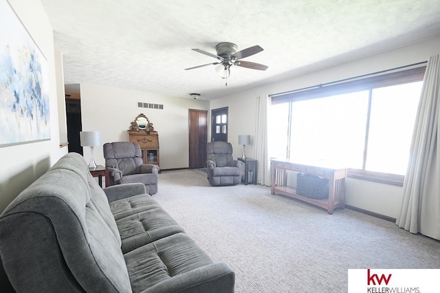 living room with ceiling fan, a textured ceiling, light colored carpet, visible vents, and baseboards