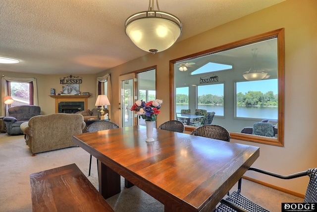 dining room with a fireplace, a water view, a textured ceiling, and light colored carpet