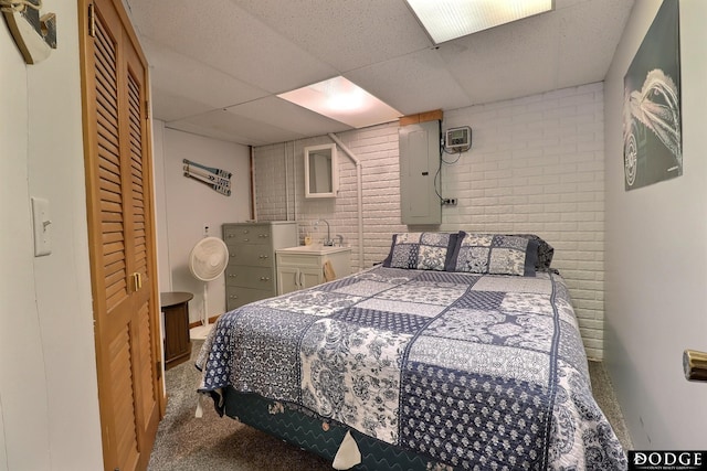 carpeted bedroom with a paneled ceiling, a sink, brick wall, and electric panel