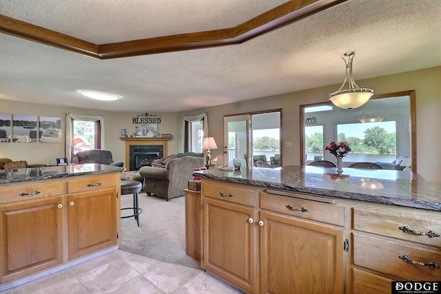 kitchen featuring light carpet, a fireplace, open floor plan, decorative light fixtures, and dark stone counters