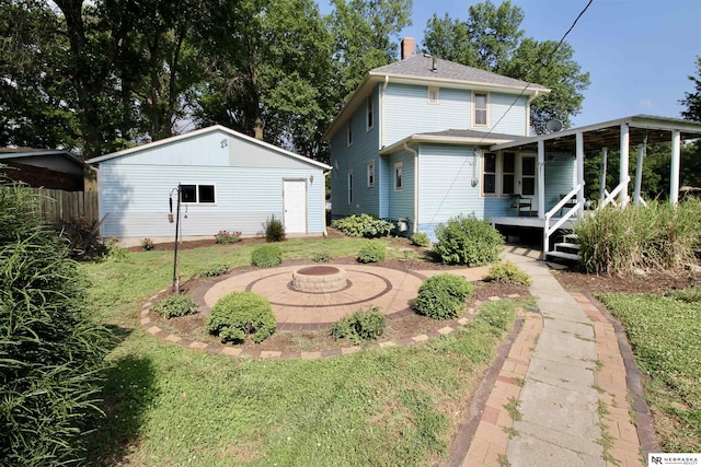 back of house featuring an outdoor fire pit, a chimney, an outdoor structure, a lawn, and a porch