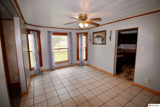 spare room featuring a ceiling fan, light tile patterned floors, crown molding, and baseboards