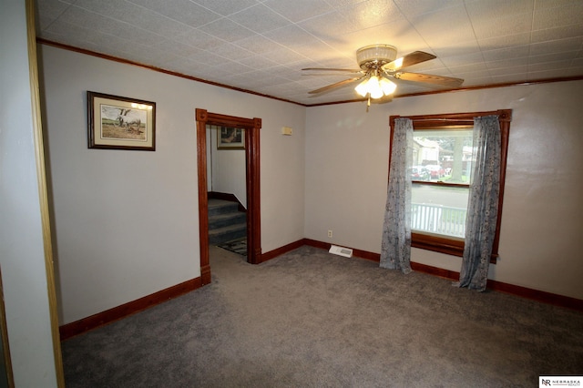 carpeted empty room with a ceiling fan, crown molding, baseboards, and visible vents