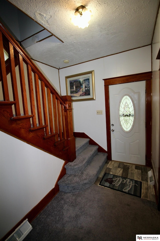 carpeted foyer entrance featuring stairs, visible vents, and a textured ceiling