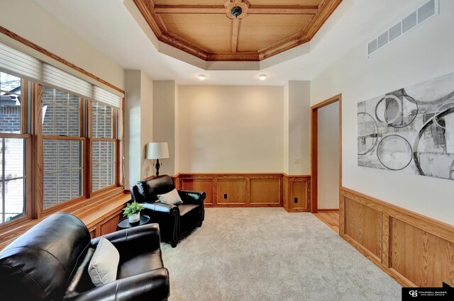 sitting room featuring a tray ceiling, wainscoting, crown molding, wooden ceiling, and light carpet