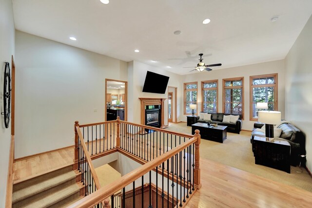 living area with recessed lighting, ceiling fan, light wood finished floors, a glass covered fireplace, and baseboards