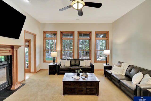 living area with a tile fireplace, light carpet, baseboards, and a ceiling fan