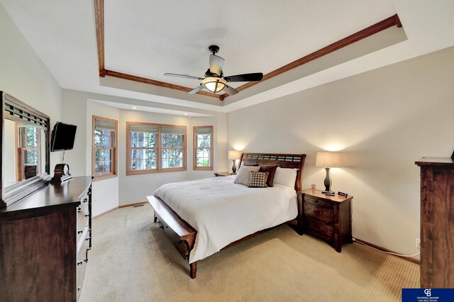 bedroom with a tray ceiling, light carpet, multiple windows, baseboards, and crown molding