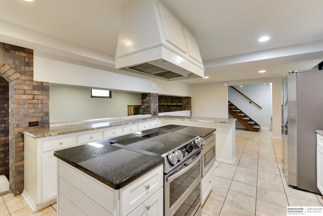 kitchen with a center island, custom range hood, white cabinets, stainless steel appliances, and light tile patterned flooring