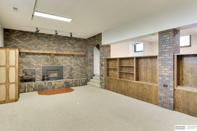 carpeted living room featuring arched walkways, rail lighting, brick wall, and visible vents